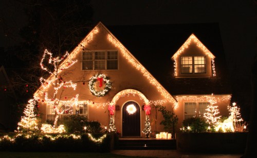 A cozy house decorated with festive lights and wreaths for the holiday season, glowing warmly at night.