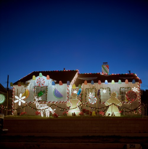 A brightly decorated house with colorful lights and festive ornaments, set against a twilight sky.