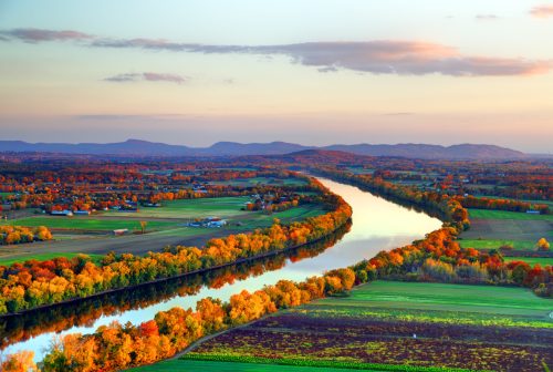 A scenic view of a winding river surrounded by vibrant autumn foliage and rolling hills under a colorful sky.