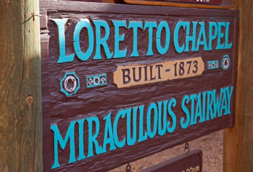 Sign for Loretto Chapel, built in 1873, featuring the words "Miraculous Stairway" in decorative lettering.