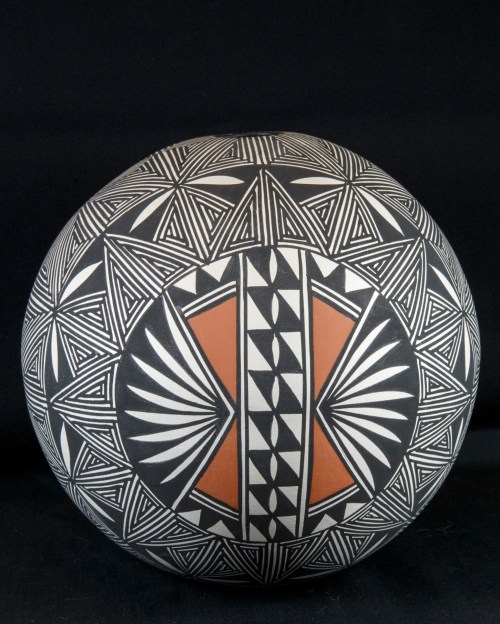 A round pottery piece featuring intricate black and white geometric patterns with a central orange design.