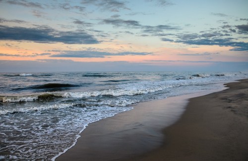 A serene beach at sunset, with gentle waves lapping at the shore under a colorful sky.