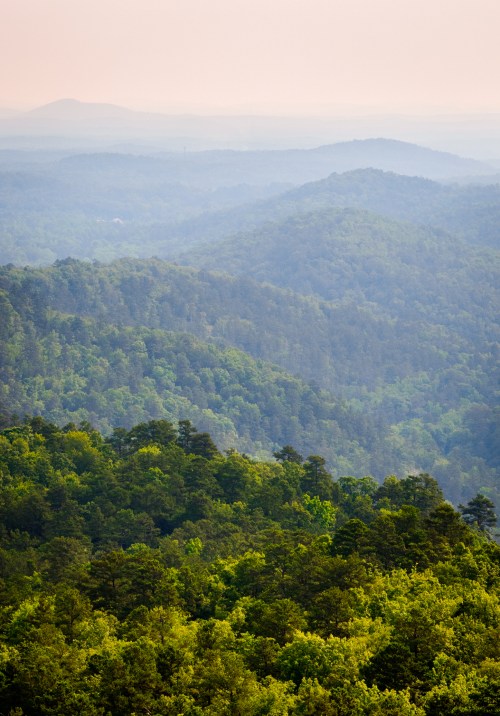 A panoramic view of lush green mountains fading into the distance under a soft, hazy sky.