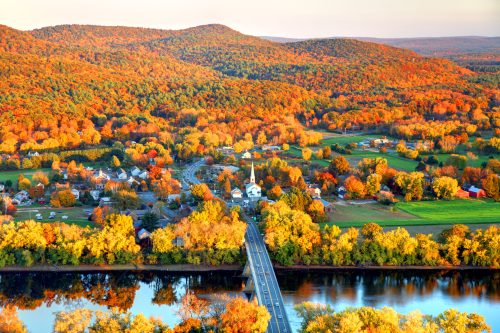 Aerial view of a vibrant autumn landscape with colorful trees, a river, and a small town nestled in the hills.