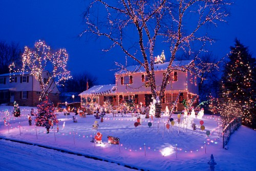 A festive house decorated with colorful Christmas lights and ornaments, surrounded by snow and holiday decorations.