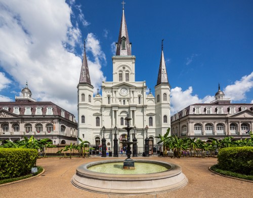St. Louis Cathedral in New Orleans, featuring tall spires and a fountain in the foreground against a blue sky.