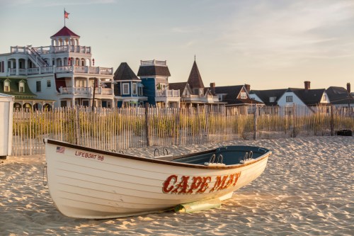 A lifeboat on the sandy beach with colorful Victorian-style houses in the background under a clear sky.