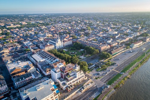 Aerial view of a city with historic buildings, green parks, and a waterfront along a river.
