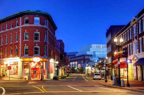 A charming street scene at dusk, featuring brick buildings, shops, and streetlights in a vibrant urban setting.