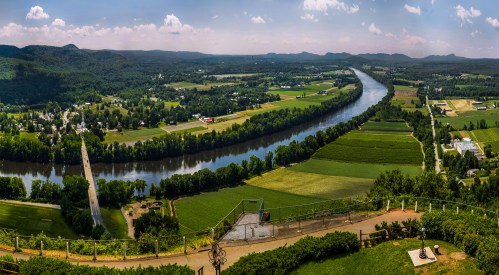A panoramic view of a river winding through lush green fields and hills under a clear blue sky.