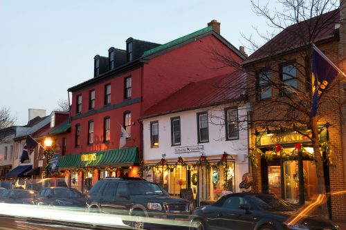 A charming street scene with festive decorations on shops and cars passing by at dusk.