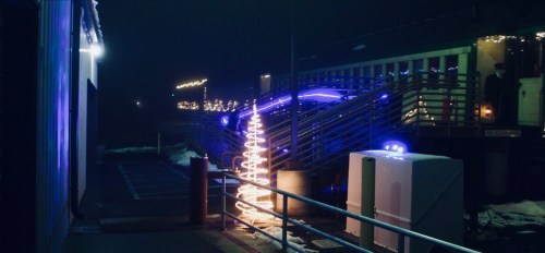 A dimly lit scene featuring colorful lights on a building and a spiral light decoration in the foreground.
