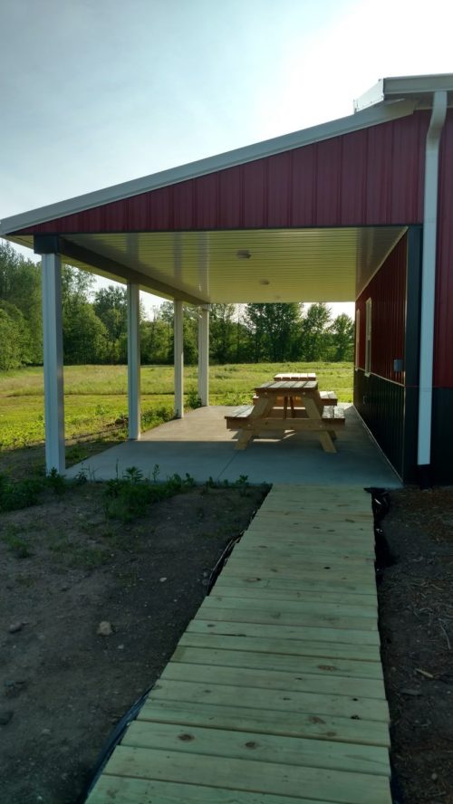 A covered patio with picnic tables, leading to a grassy field and trees in the background.