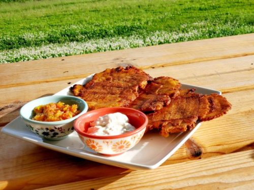 A plate of golden-brown fried plantains served with two colorful bowls of dipping sauces on a wooden table.