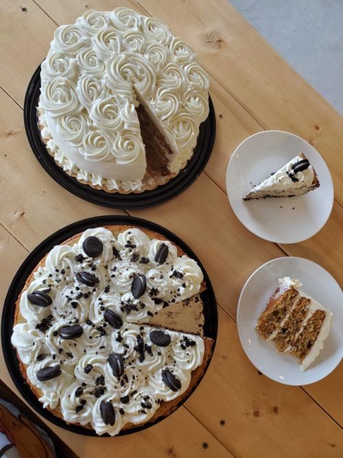 Two cakes on a wooden table: one round with white frosting and rosettes, the other with Oreo toppings and slices removed.