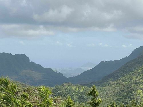 A scenic view of lush green mountains with a distant coastline under a cloudy sky.