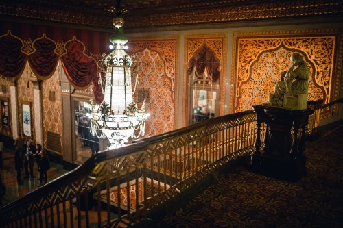 Elegant interior with ornate walls, a grand chandelier, and a statue, capturing a luxurious atmosphere.