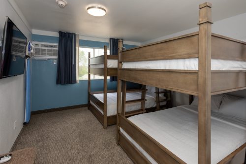 A cozy room featuring two sets of wooden bunk beds, a TV, and an air conditioning unit by the window.