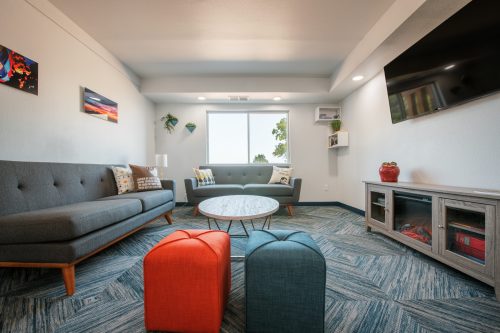 A modern living room with a gray sofa, colorful ottomans, a round coffee table, and a wall-mounted TV.