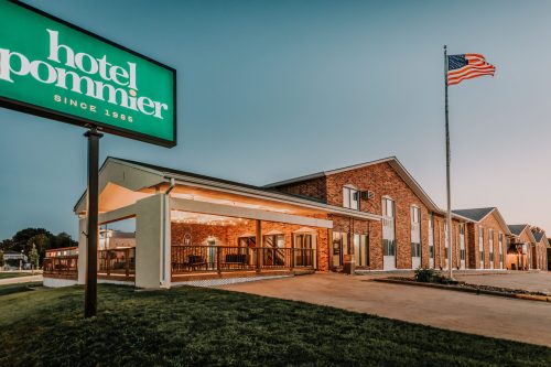 Exterior of Hotel Ponnmier at dusk, featuring a sign, American flag, and well-lit outdoor seating area.
