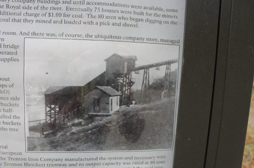 Historic black-and-white photo of a coal mine and company store, showcasing mining infrastructure by a river.