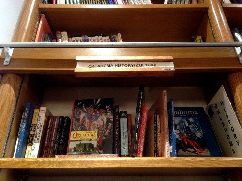 Bookshelves filled with various books on Oklahoma history and culture, labeled clearly above.
