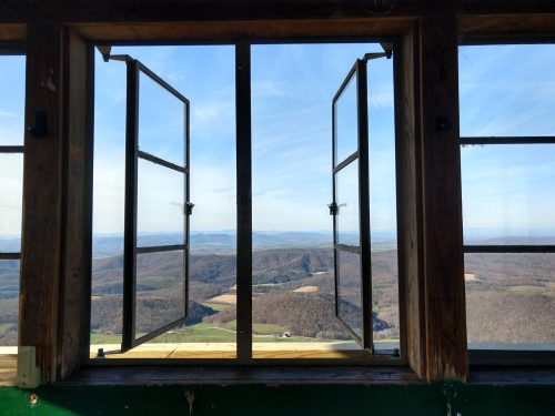 Open windows frame a scenic view of rolling hills and valleys under a clear blue sky.