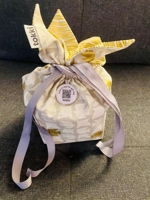 A wrapped gift with a patterned fabric and ribbon, sitting on a gray couch.