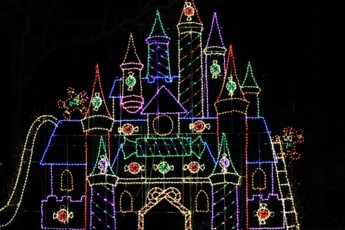 A brightly lit castle made of colorful Christmas lights against a dark night sky.