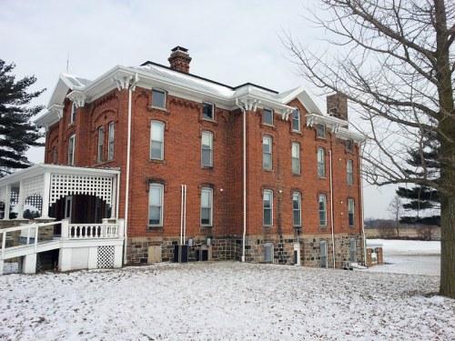 A large, historic brick house with white trim, surrounded by snow and trees, showcasing a classic architectural style.