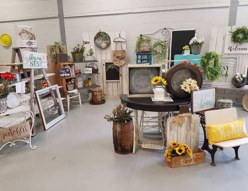 A cozy shop display featuring rustic decor, signs, and floral arrangements in a bright, open space.