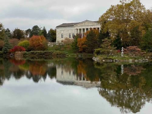 A serene lake reflects a historic building surrounded by colorful autumn foliage.