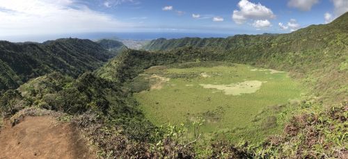 A panoramic view of a lush green valley surrounded by mountains under a blue sky with scattered clouds.