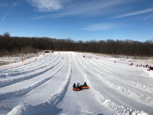 A snowy tubing hill with multiple lanes, people tubing, and a clear blue sky in the background.