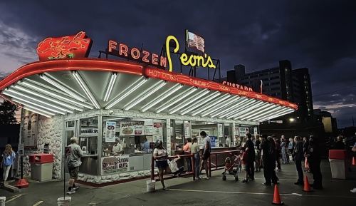 A retro ice cream stand with neon lights, bustling with customers in the evening.