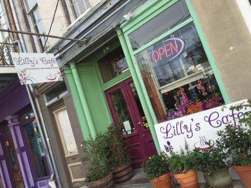 A colorful café exterior with signs reading "Lilly's Café" and "OPEN," surrounded by potted plants.