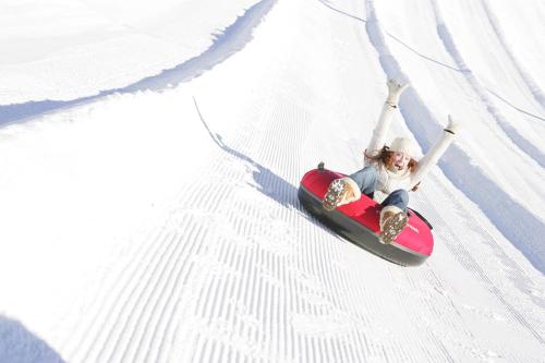 A person joyfully sledding down a snowy slope, arms raised in excitement, on a red inflatable tube.
