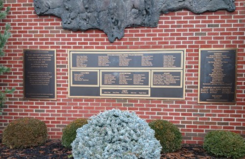 A brick wall featuring plaques with names and honors, surrounded by greenery.