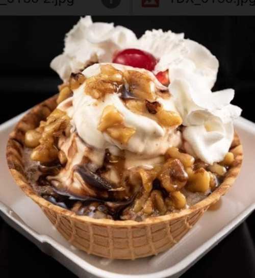 A delicious ice cream sundae in a waffle bowl, topped with whipped cream, nuts, and a cherry.