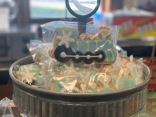 A metal tray filled with decorated cookies shaped like a train and snowflakes, all individually wrapped.