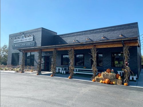 A black brick building with a porch decorated with pumpkins and hay bales, under a clear blue sky.
