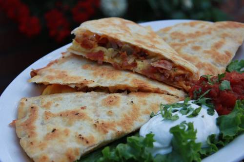 A plate of quesadillas filled with cheese and ham, served with salsa, sour cream, and fresh lettuce.
