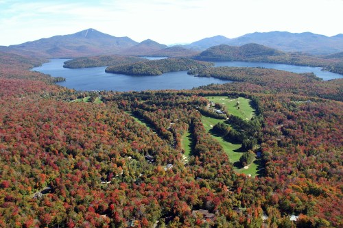 Aerial view of a vibrant autumn landscape with colorful trees, a lake, and mountains in the background.