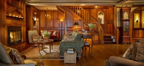 Cozy living room with wooden walls, a fireplace, elegant furniture, and a staircase in a warm, inviting atmosphere.