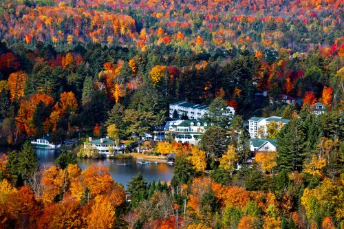 A vibrant autumn landscape featuring colorful trees, a serene lake, and charming buildings nestled among the foliage.