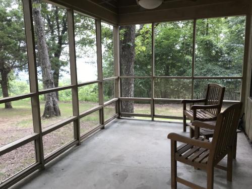 A screened porch with two wooden chairs, surrounded by trees and a view of greenery outside.