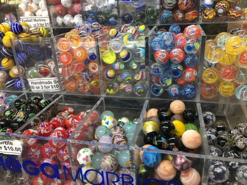 A colorful display of various marbles in clear containers, showcasing different designs and sizes.
