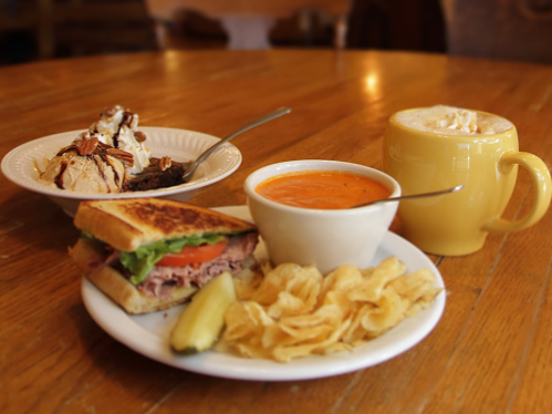 A plate with a sandwich, chips, and a bowl of tomato soup, alongside a dessert and a cup of hot beverage.