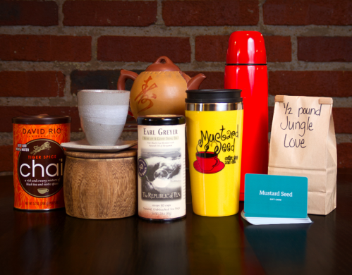 A collection of tea and coffee items, including cans, a teapot, mugs, and a gift card, arranged on a wooden surface.
