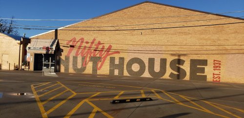 Mural on a brick building reading "Milty's No House" with "EST. 1937" in bold letters. Clear blue sky above.
